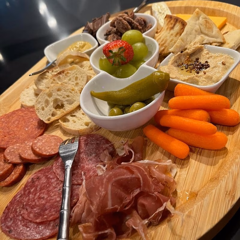 Charcuterie board with meats, bread, cheeses, vegetables, fruits, and dips.