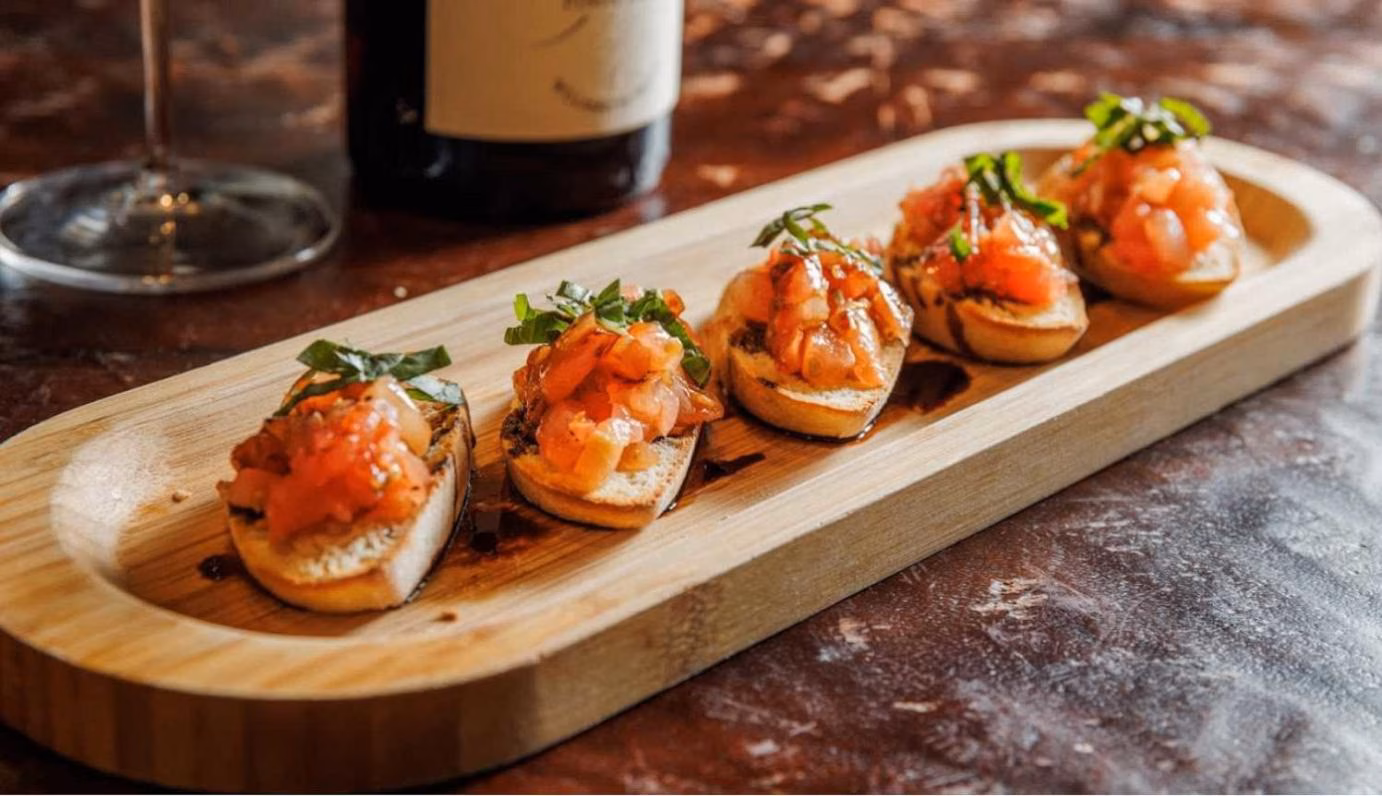 Five pieces of tomato bruschetta with herbs on a wooden tray.