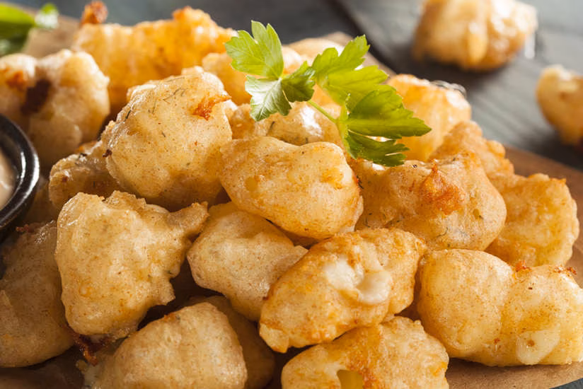 Close-up of golden-brown fried cheese curds with a parsley garnish.