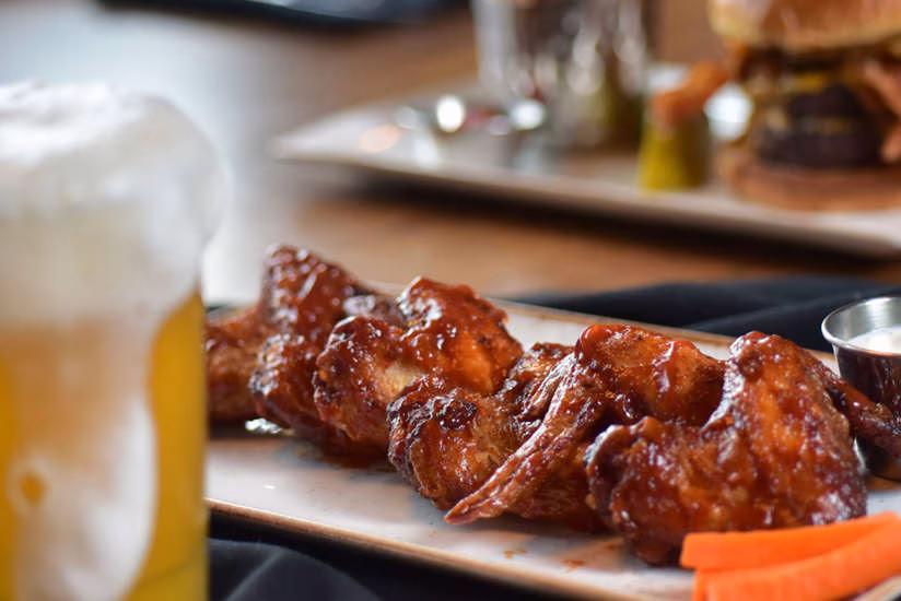 Plate of glazed chicken wings with frothy beer and dipping sauce.