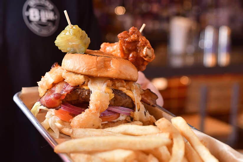 Large burger with fries, pickle, and chicken wing on a metal tray.