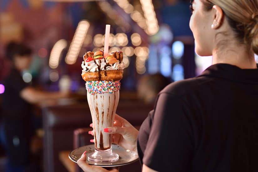 Woman holding an elaborate milkshake with a donut and mini burgers.