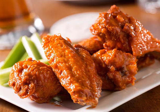 Buffalo chicken wings with celery sticks on a white plate.