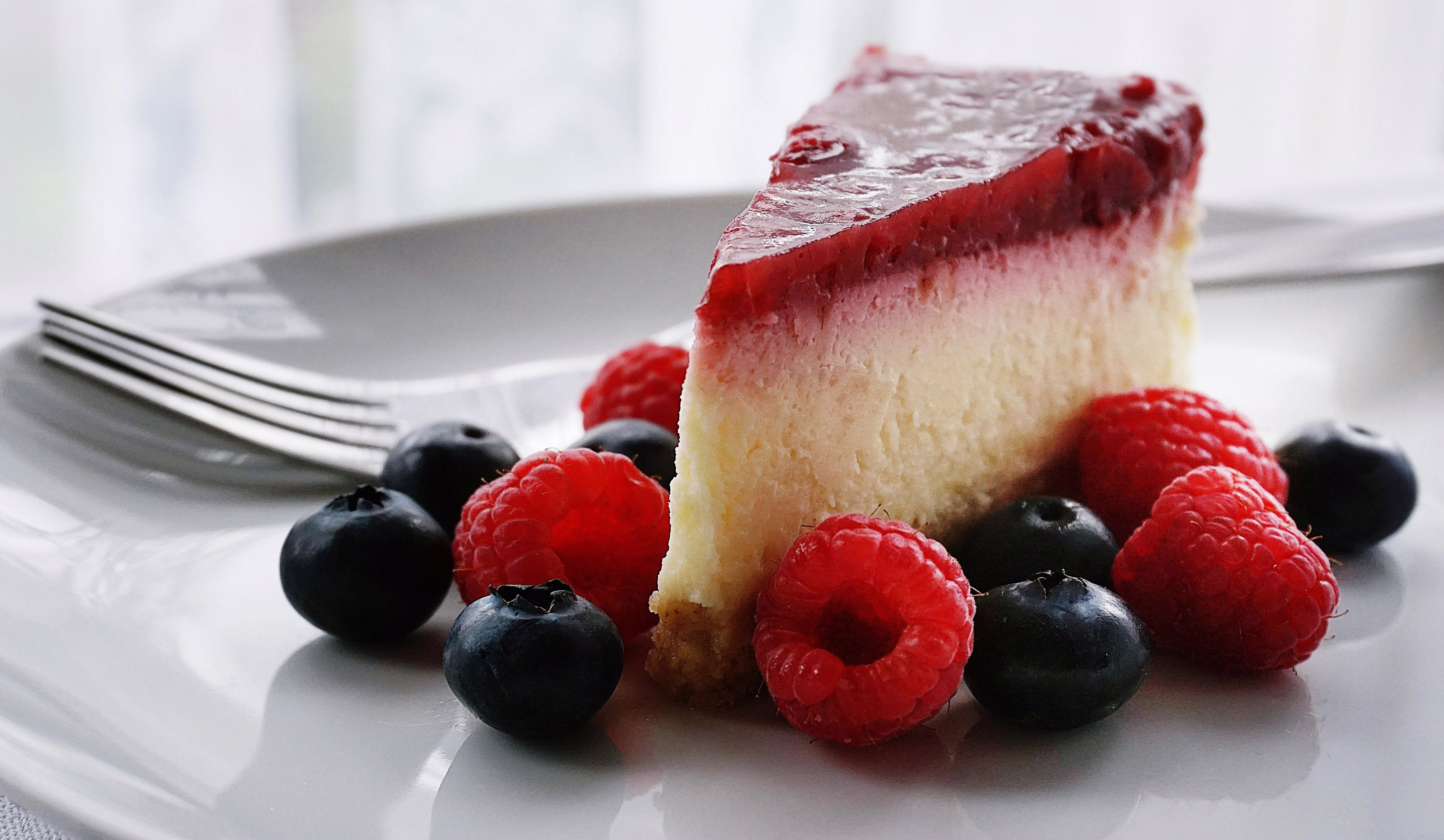 Slice of cheesecake with red berry topping, fresh raspberries, and blueberries.