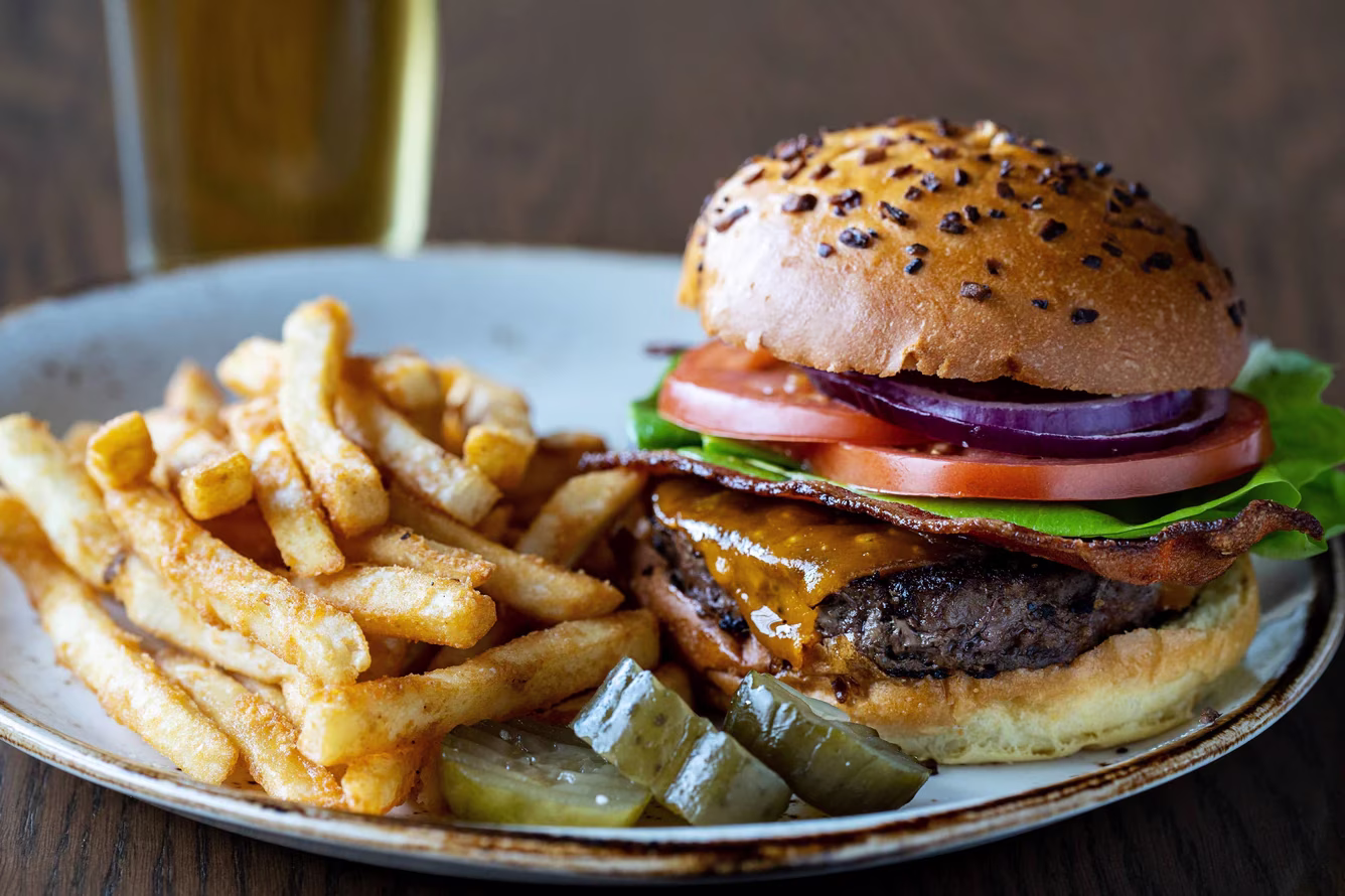 Cheeseburger with bacon, fries, and pickles on a plate.