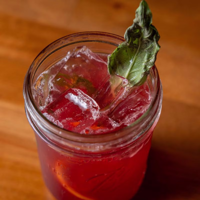 Red iced drink with basil leaf garnish in a mason jar.