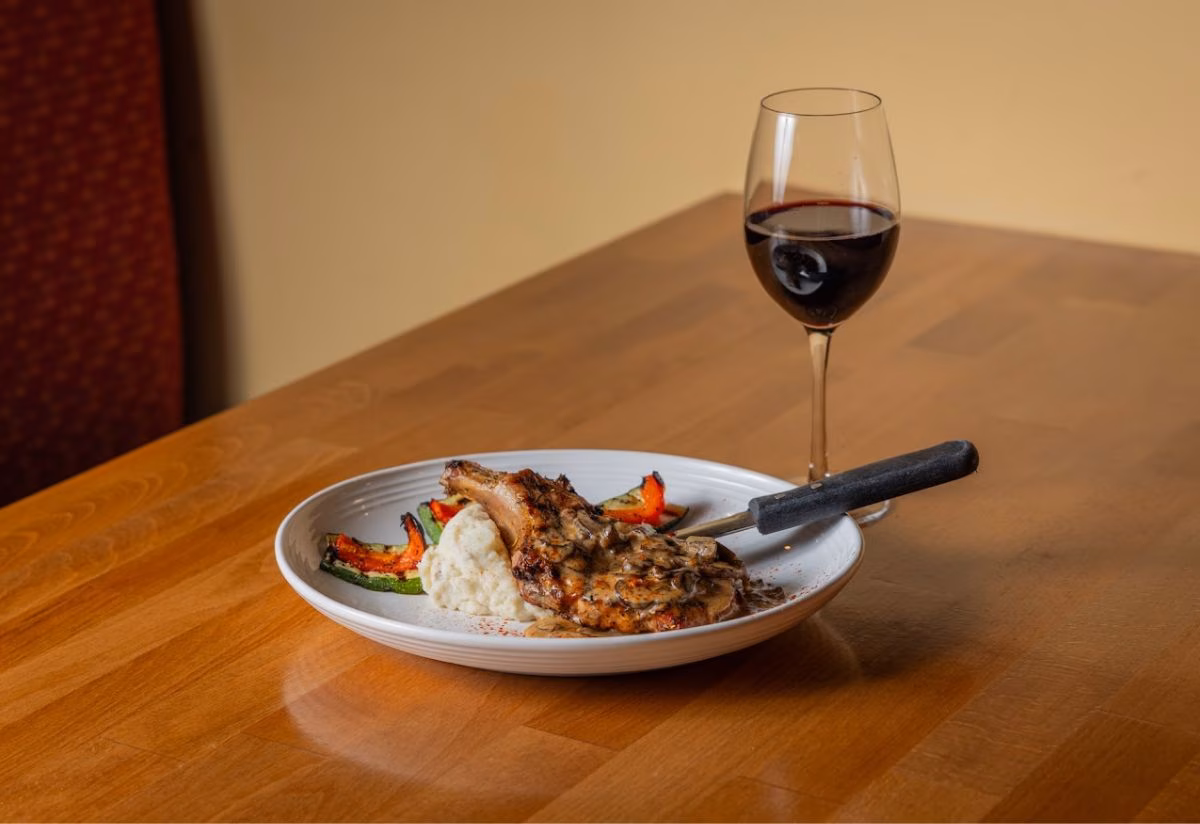Plate with pork chop, mushroom sauce, mashed potatoes, vegetables, and red wine.
