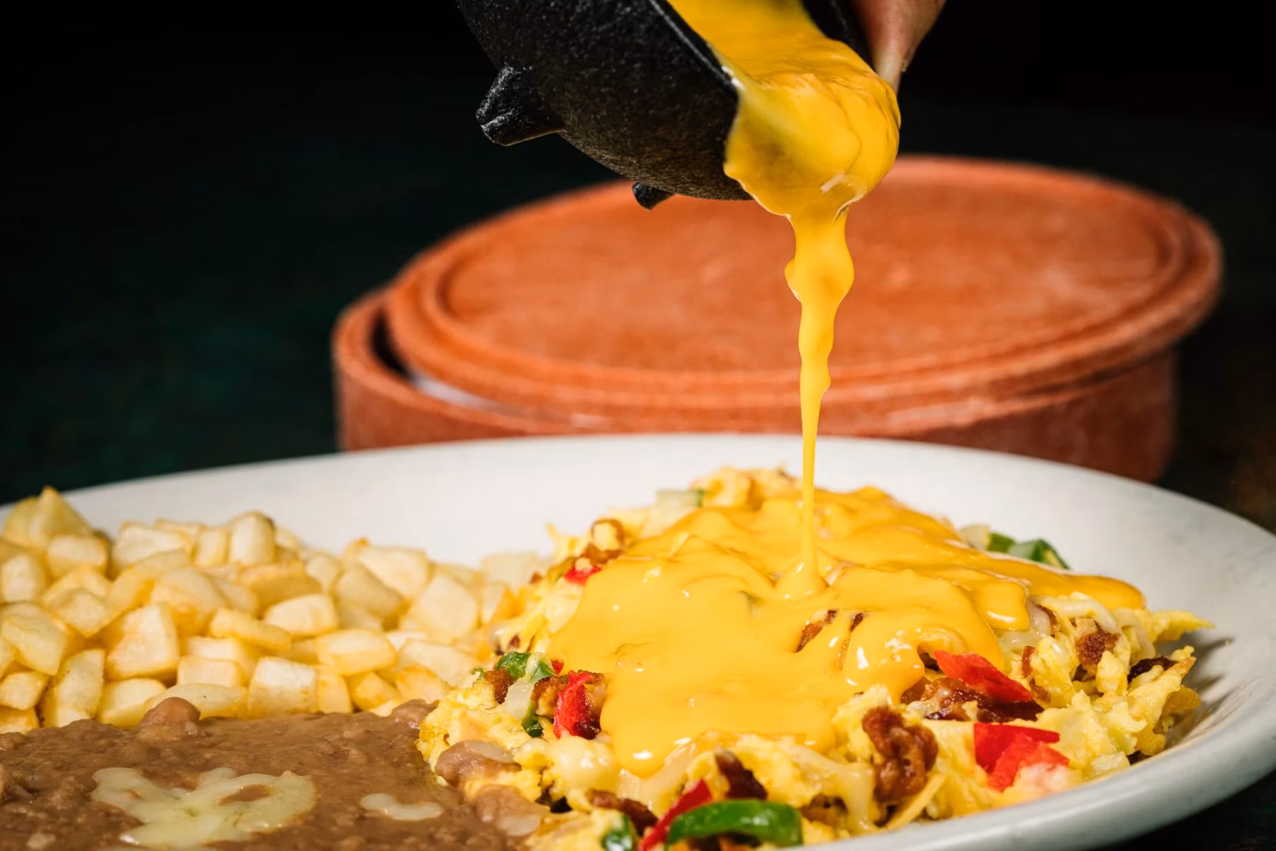 Yellow cheese sauce poured onto scrambled eggs, beans, and potatoes.