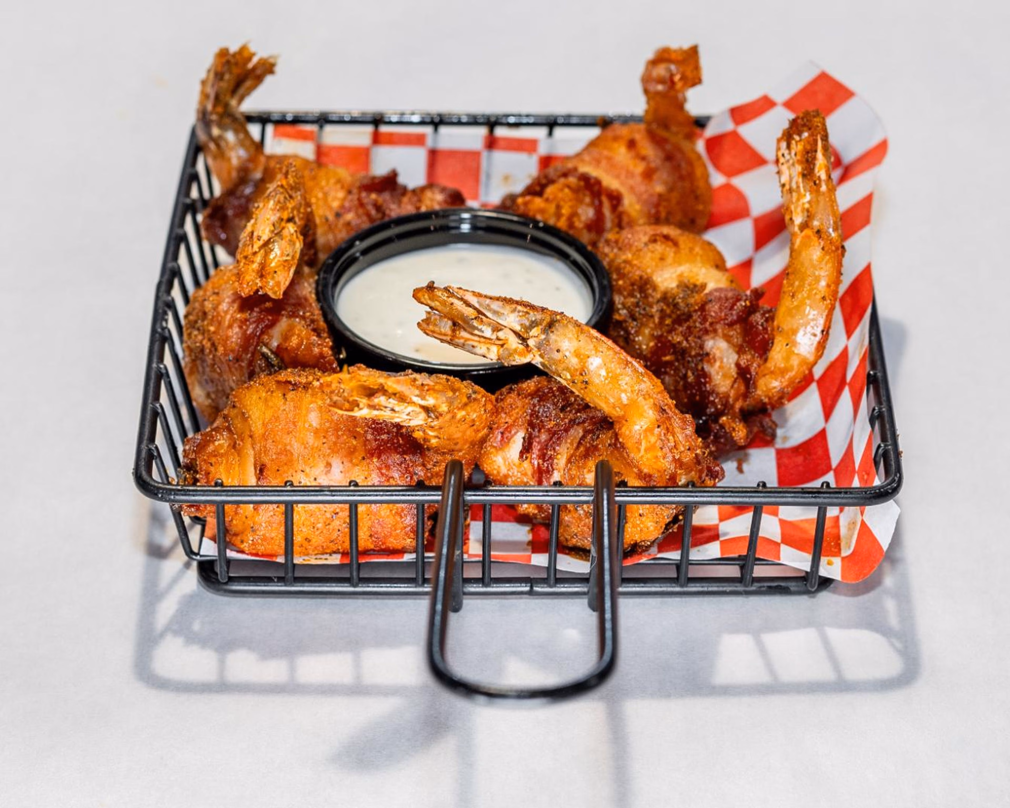 Crispy, seasoned, wrapped shrimp with white dipping sauce in a basket.