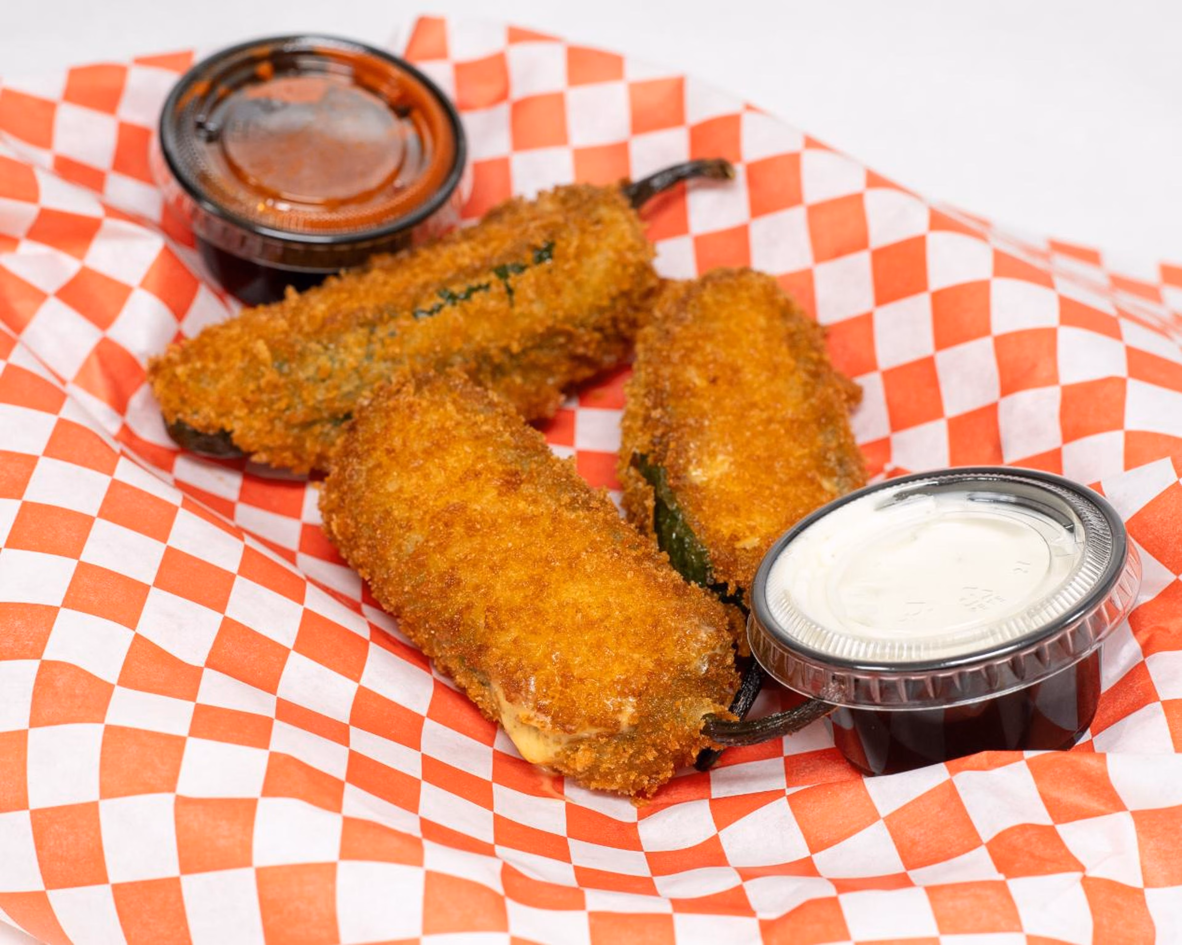 Three golden-brown deep-fried peppers with two dipping sauces.