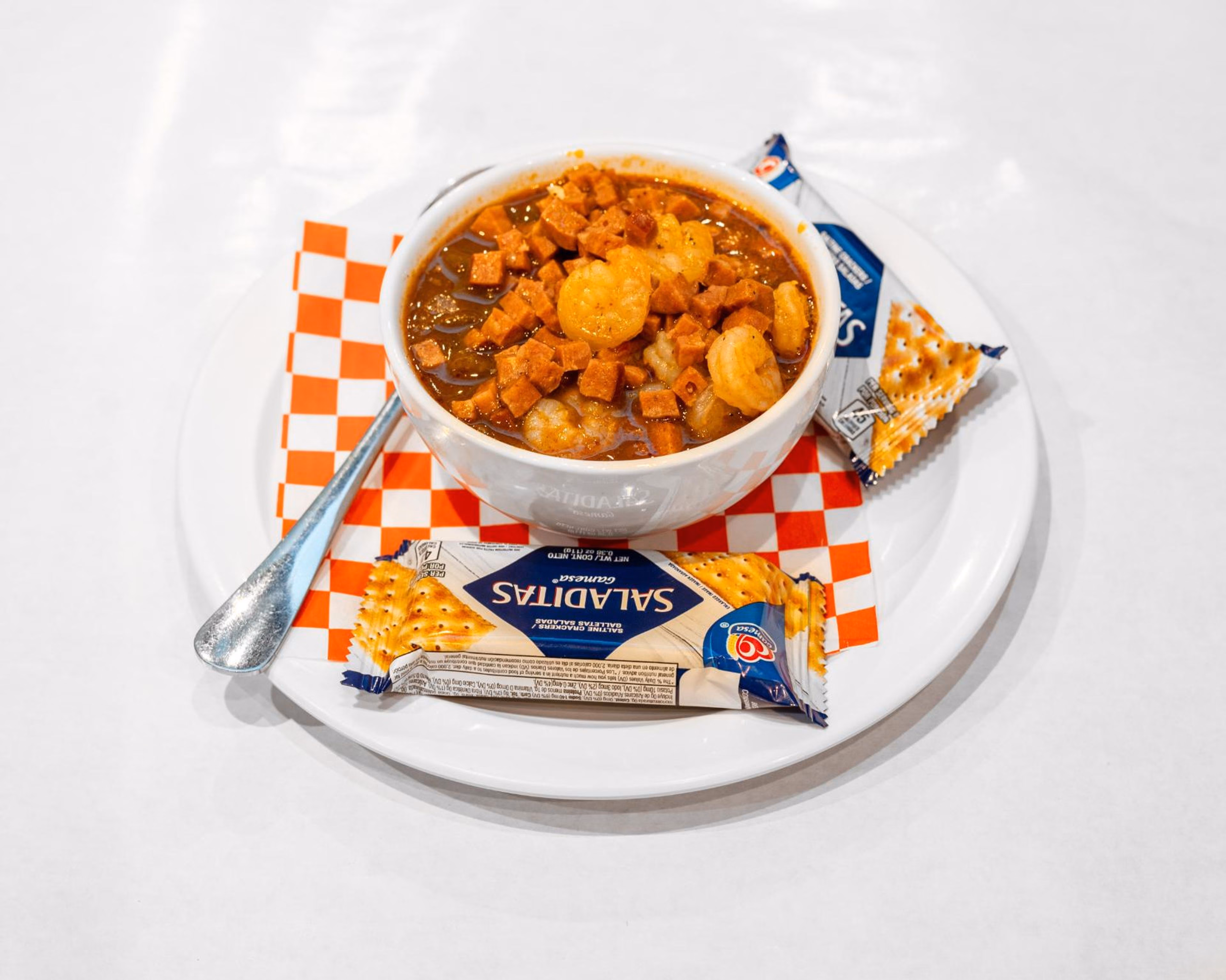 Shrimp and sausage stew, crackers, spoon, and checkered paper liner.