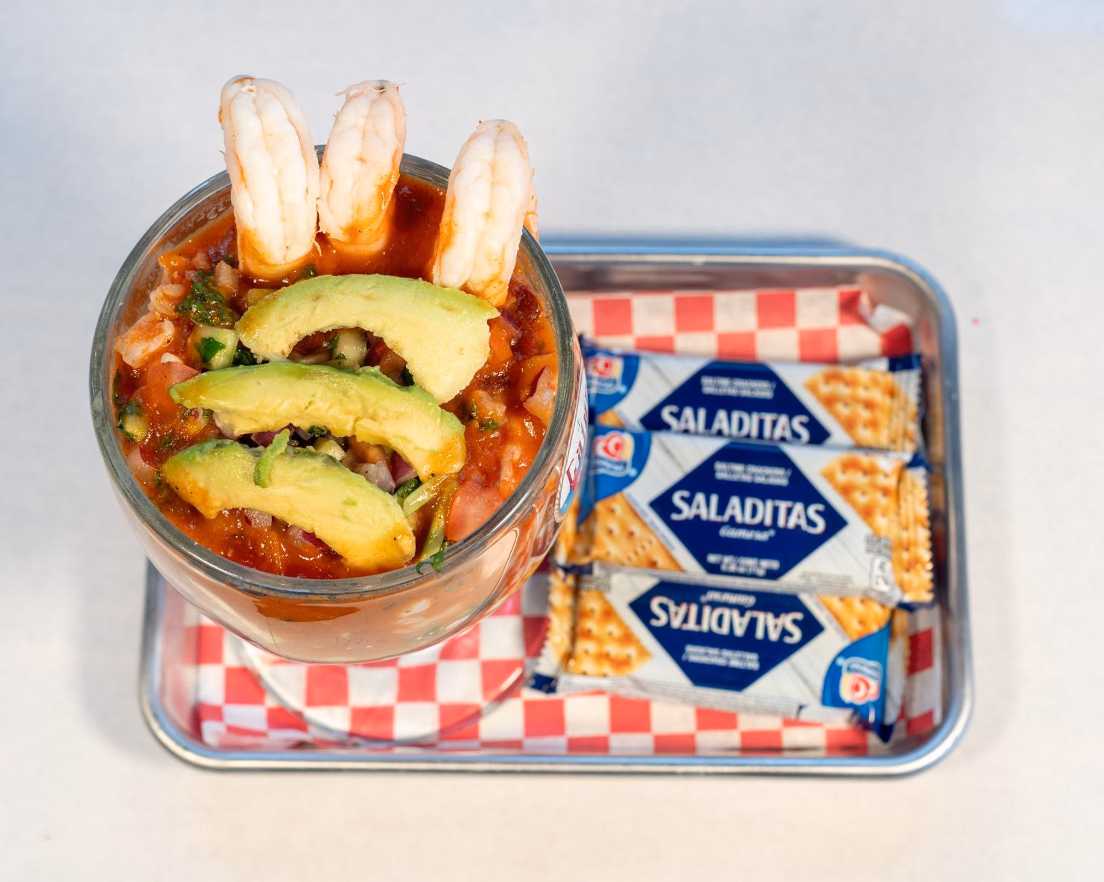 Shrimp cocktail with avocado, served with crackers on a tray.