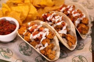 Three fried tacos with toppings, tortilla chips, and red salsa.