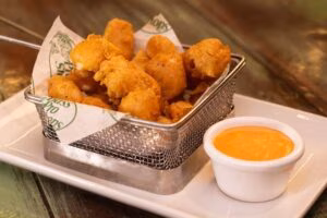 Golden fried bites in metal basket with orange dipping sauce.