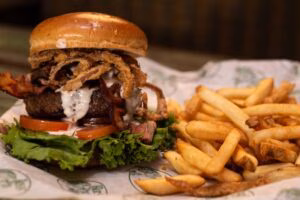 Burger with bacon, crispy onions, lettuce, tomato, and fries.