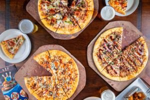 Three pizzas, some with slices removed, plus drinks and food.