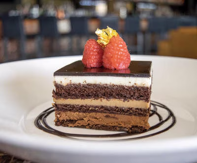 Layered chocolate cake with raspberries and gold leaf on a white plate.