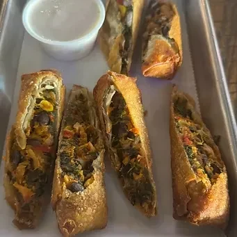 Six deep-fried rolls cut open, showing colorful filling and dipping sauce.