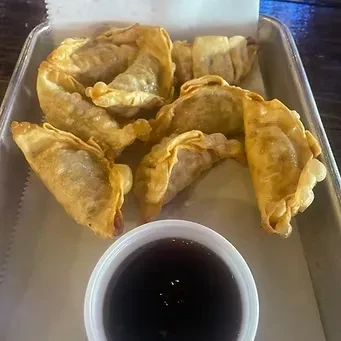 Golden-brown fried dumplings with crimped edges, in a tray with dipping sauce.