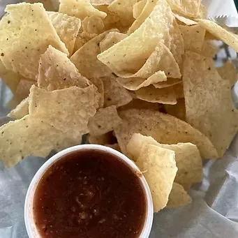 Crispy golden tortilla chips in a basket with chunky red salsa.