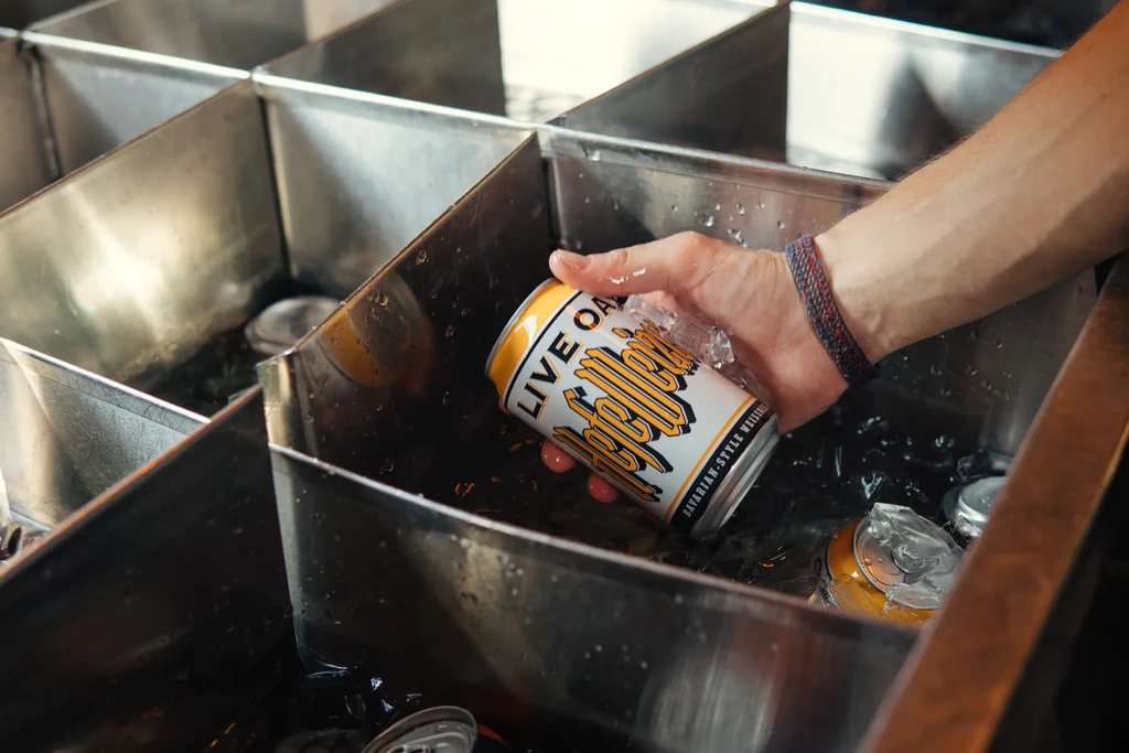 Hand retrieves a Live Oak HefeWeizen can from an ice bin.