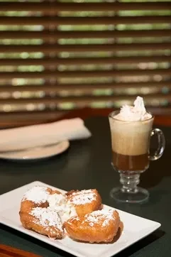 Three sugar-dusted fried dough pieces and a whipped cream coffee.