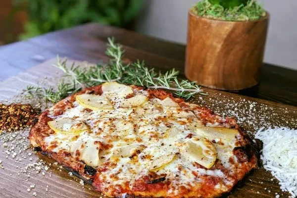 Gourmet pear pizza with cheese, rosemary, and chili flakes on wood.