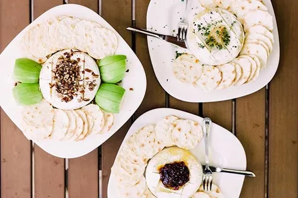 Three baked cheese appetizer plates with crackers and varied toppings.