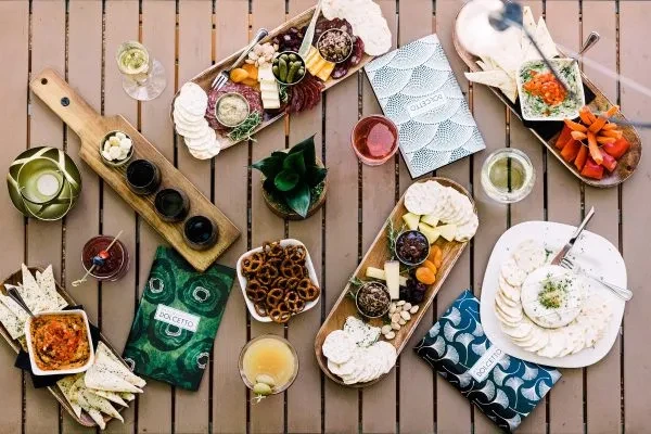 Overhead charcuterie, dips, and drinks with Dolcetto branding on a table.