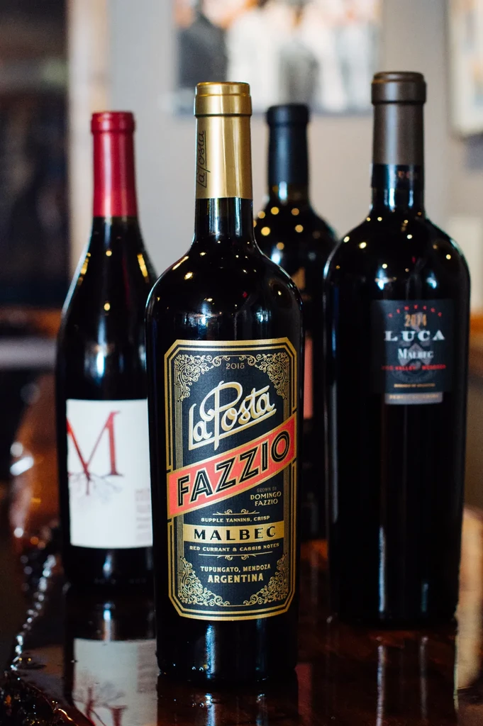 Four dark wine bottles, La Posta Fazzio Malbec prominent, on a reflective surface.