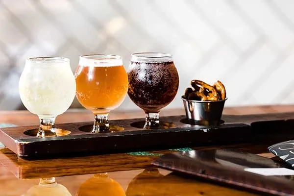 Three beers, light to dark, with pretzels on a wooden paddle.