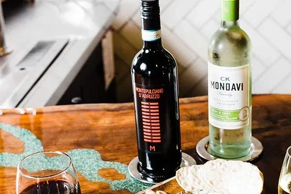 Wine bottles, red wine glass, and cracker on a turquoise resin table.