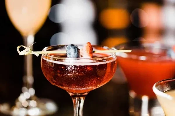 Reddish-pink cocktail in a coupe glass with berry skewer.