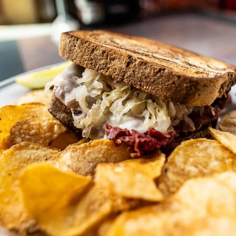 Close-up: Reuben sandwich on rye with chips and a pickle.