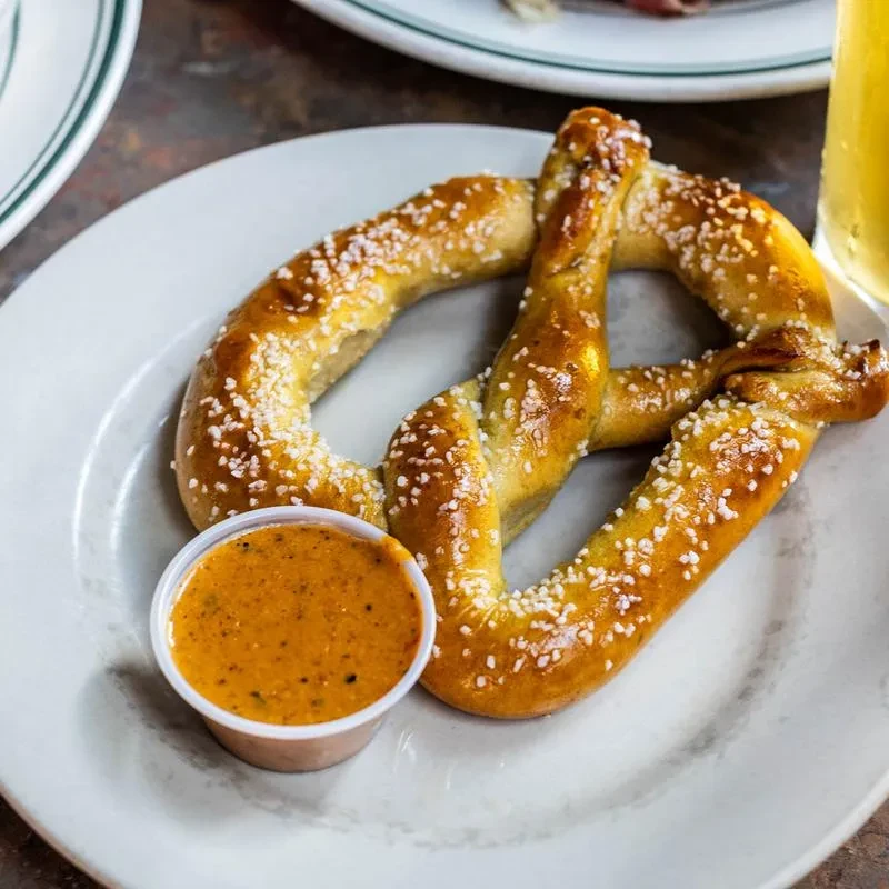 Golden-brown soft pretzel with salt and reddish-orange dipping sauce.