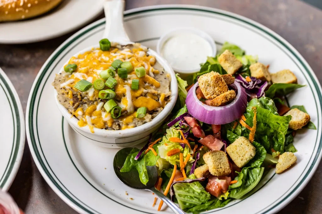 Cheesy potato casserole, green salad, and dressing on a diner plate.