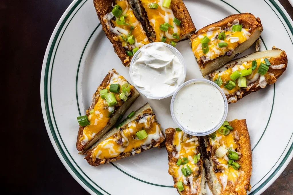 Loaded potato wedges with melted cheese, green onions, and dips.