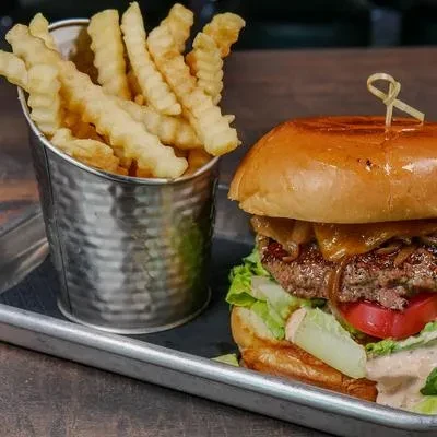 Close-up of a burger with melted cheese and crinkle-cut fries on a tray.
