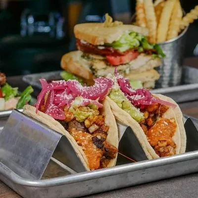 Two tacos, a stacked sandwich, and fries on a metal tray.