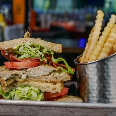 Stacked club sandwich and crinkle-cut fries on a grey tray.