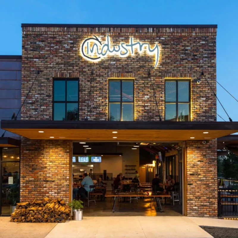 Modern-industrial 'Industry' restaurant at dusk with bright neon sign.