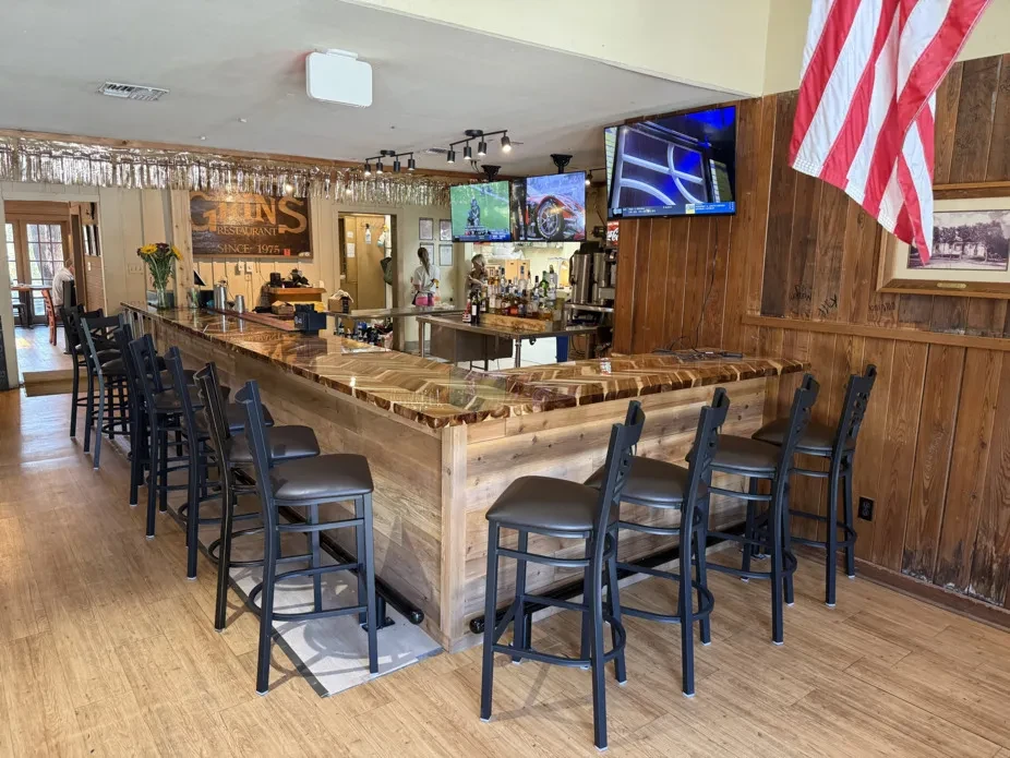 Rustic Grins Restaurant bar with U-shaped wooden bar, stools, and TVs.