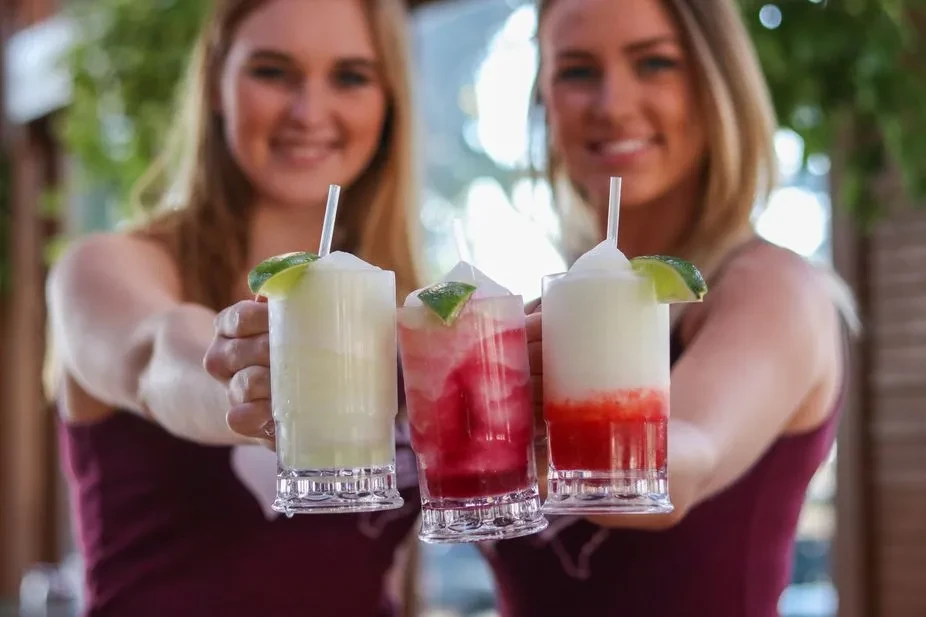 Three frosted drinks with lime wedges held by blurred smiling women.
