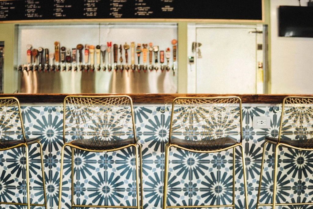 Modern bar with four gold-framed stools, patterned tiles, and beer taps.
