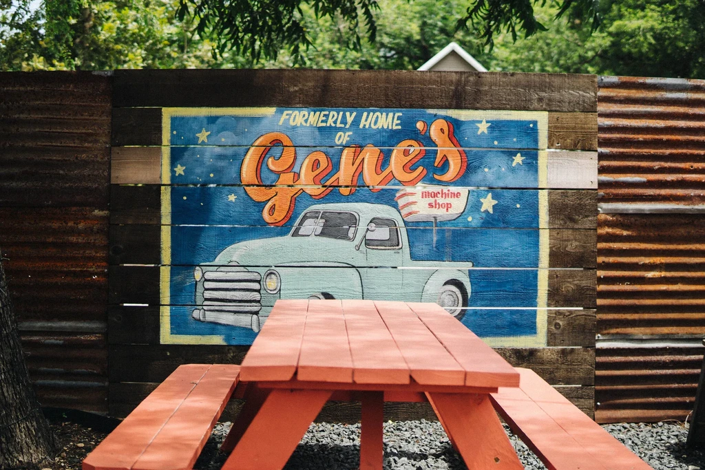 Orange wooden picnic table in front of a vintage blue truck mural.