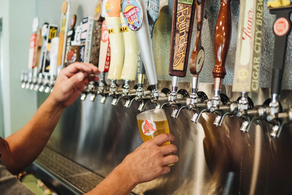 Hands pouring golden beer from a draft tap into a branded glass.