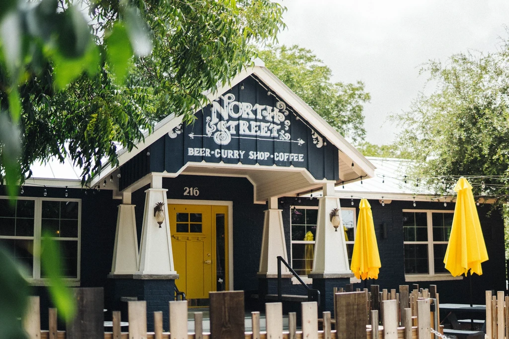 Exterior of North Street Beer Curry Shop Coffee, yellow doors and patio.