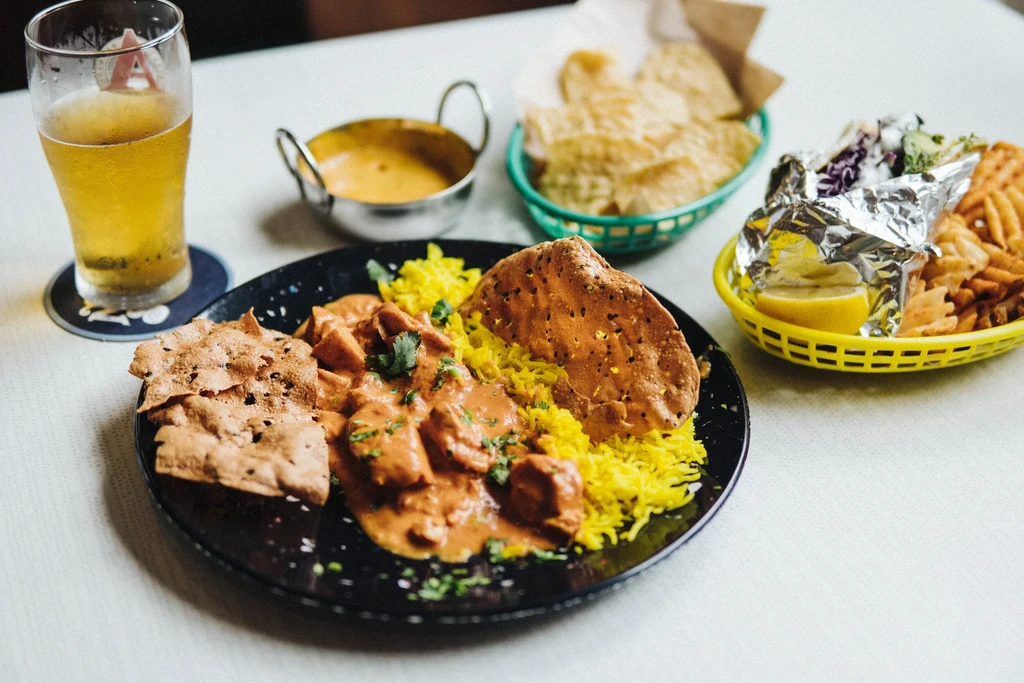 Black plate of orange curry, yellow rice, pappadums, beer, and fries.
