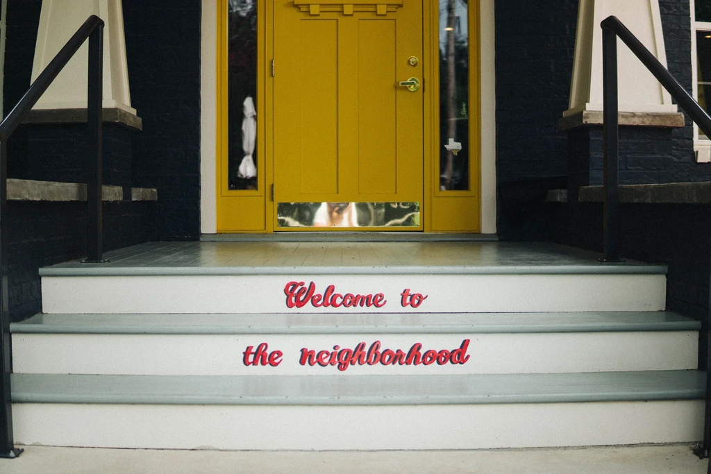 Mustard-yellow double doors and white steps reading 'Welcome to the neighborhood'.