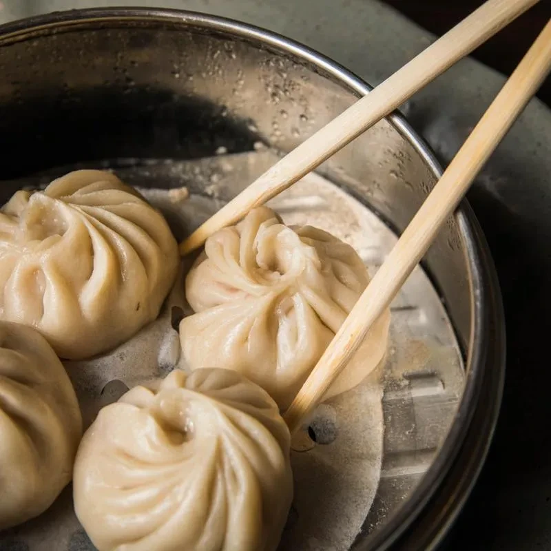 Four pleated steamed dumplings in a hot metal steamer with chopsticks.